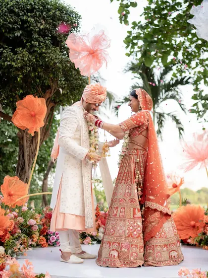 The Varmala exchange, a playful and significant ritual. This shot captures the couple's interaction against their stunning outdoor floral decor.