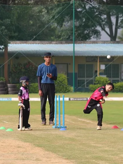 A young bowler in action during a U-10 match, with an umpire observing the delivery.
