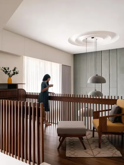 **Amber House, Ahmedabad:** The upper-level passage overlooks the main living area, maintaining a sense of connection between floors. The wooden railings continue the theme of vertical lines, creating visual rhythm and a feeling of warmth and craftsmanship.