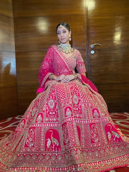 A full view of this regal bridal look. The model's modern, subdued makeup is the perfect complement to the traditional and heavily embroidered pink lehenga.