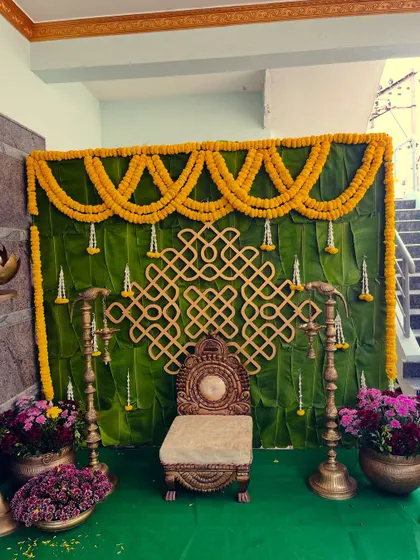 A simple and elegant Haldi backdrop featuring a wall of banana leaves. The decor is accented with marigold garlands and a traditional kolam-style cutout, creating a truly authentic look.