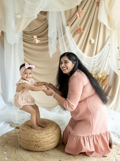 A mother helps her little girl balance on a pouf. This playful and supportive interaction is a wonderful moment to capture.