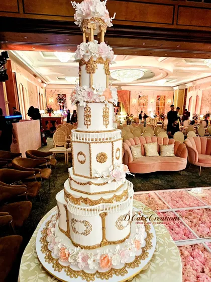 Another perspective of the grand architectural cake, showcasing its intricate details against the backdrop of the elegant event space. The lighting highlights the gold accents and the texture of the sugar work.