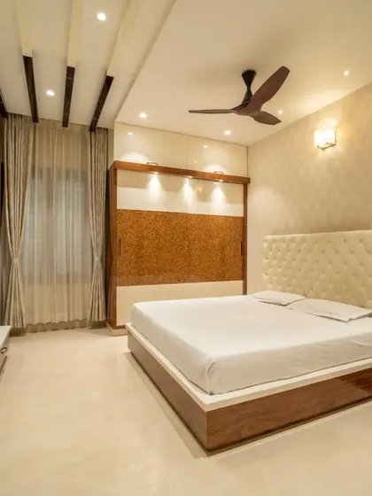 A serene bedroom with a tufted cream headboard, complemented by wood paneling and soft, ambient lighting.