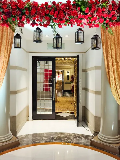 A simple yet elegant entranceway featuring golden drapes, hanging lanterns, and an overhead garland of red flowers. This design adds a touch of warmth and traditional charm to the venue's doorway.