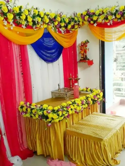 A decoration setup for a Ganpati pooja at home. The mandap is created with colorful drapes and decorated with yellow flower garlands, providing a beautiful space for the idol.