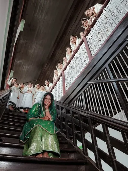 A unique, low-angle shot looking up a traditional wooden staircase at the bride and her family during the Arikuth ceremony.