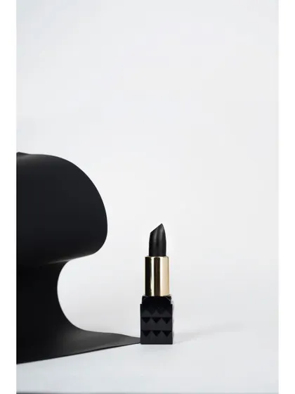 A minimalist product shot of a black lipstick next to an abstract black sculpture against a stark white background. This high-concept, artistic photo is ideal for a modern cosmetics brand's campaign.