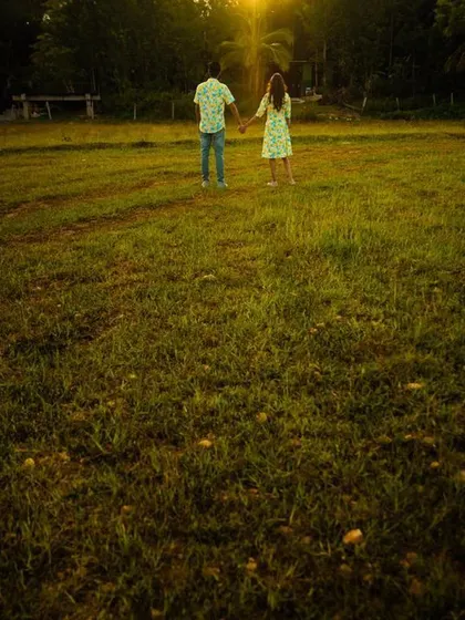 A wide shot capturing the couple holding hands in a vast green field at sunset. This image emphasizes the scale of nature and the intimacy of the couple within it.