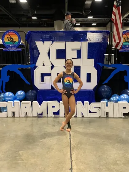This Xcel Gold athlete stands proudly in front of the championship banner after a successful competition season.