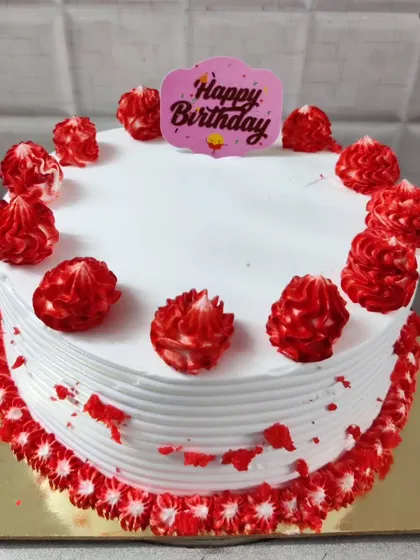 A white birthday cake with bright red piped decorations. The simple design is festive and cheerful.