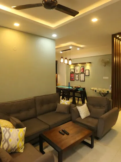 A comfortable and inviting living room with a brown sofa and a view into the adjacent dining area. The space is painted in a soothing pastel green, creating a relaxed atmosphere.