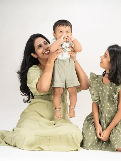 A mother and her two children in a clean, simple studio setting. The focus is entirely on their happy expressions and the bond they share.