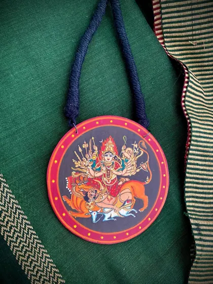The Durga Mahishasuramardini pendant, a miniature masterpiece of divine power, set against a rich green fabric.