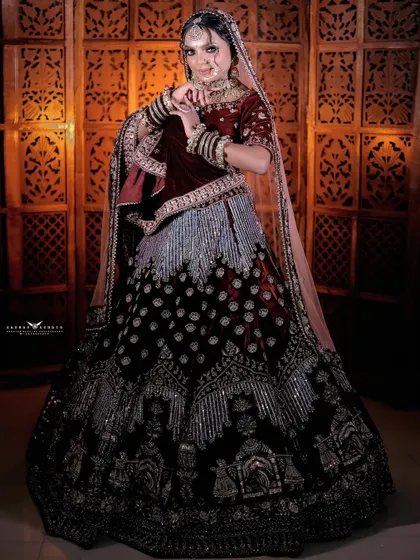 A full-length shot of a bride in a magnificent maroon velvet lehenga. The skirt features a unique doli (palanquin) embroidery, telling a story within the outfit itself.