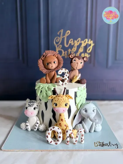 A safari cake for Om's birthday, featuring a whole crew of adorable, hand-sculpted jungle animals like a lion, monkey, zebra, and elephant.
