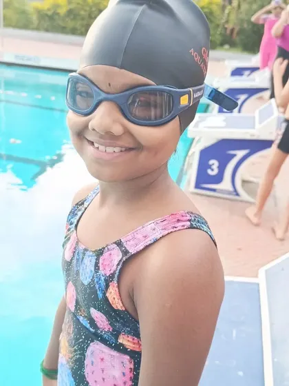 A young swimmer smiles confidently by the starting block during time trials.