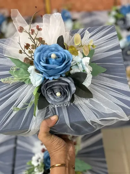 Holding up one of the finished corporate gift boxes. The combination of the dusty blue and grey tones with the delicate floral arrangement creates a sophisticated and memorable gift.