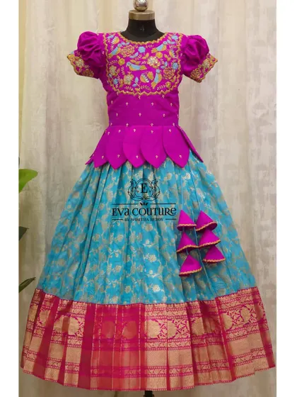 A stunning Banarasi Pattu lehenga in magenta and turquoise. The blouse features intricate bird-motif embroidery, and the skirt has a beautiful gold zari border.