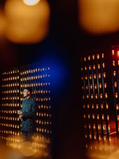 The groom stands against a dramatic wall of candles, a simple yet powerful backdrop for a stunning portrait.