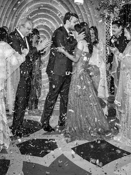 A black and white shot capturing the climax of the ring ceremony, with the couple sharing a kiss under a shower of confetti.
