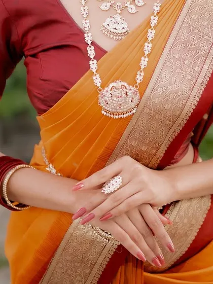 A close-up on the bride's hands and torso, showing the beautiful layering of her saree, the traditional bangles, and the elegant drape of the fabric.
