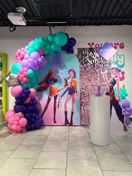 A vibrant K-pop themed birthday decoration. This setup uses a bright color palette, a shimmer wall, and cutouts of anime-style pop stars to create a fun, concert-like feel.