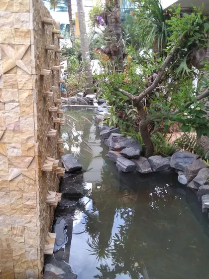 A cascading stone wall water feature creates a natural waterfall effect, flowing into a custom-built pond surrounded by rocks and lush plants.