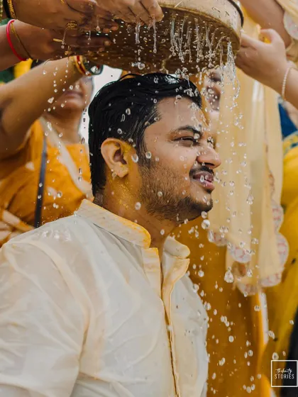 The groom is showered with water during the Haldi ceremony, a refreshing and joyful ritual captured in motion.