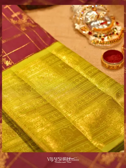 A close-up of the rich lime green zari border against the checked wine-colored body.