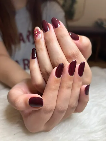 The darks are out already! A rich, glossy maroon manicure on natural nails with a single accent nail featuring a delicate 3D flower.