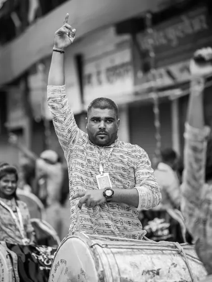 A powerful black and white portrait of a dhol player giving a signal, his arm raised high.