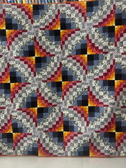 A fiery and dramatic quilt with a complex, interlocking pattern in shades of red, orange, and grey.