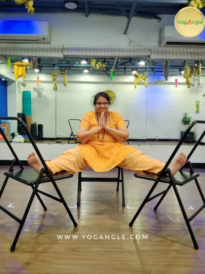 Yoga is for everyone, even those who cannot sit on the floor. This student demonstrates a wide legged seated pose using two chairs, showcasing how we adapt practices to meet individual needs and make yoga truly accessible.