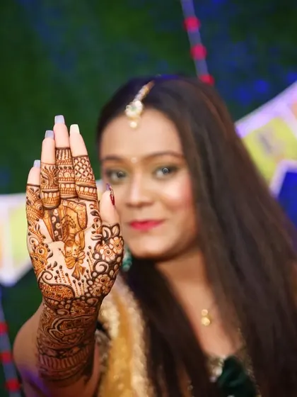 A happy Maharashtrian bride showcasing her detailed mehndi. The design includes a portrait of the groom, blending personalization with traditional patterns.