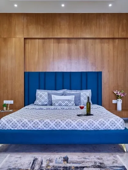 A bold and beautiful bedroom design. The royal blue upholstered bed stands out against the warm wood-paneled wall, creating a look that is both modern and timeless. The minimalist wall sconce adds an artistic touch.