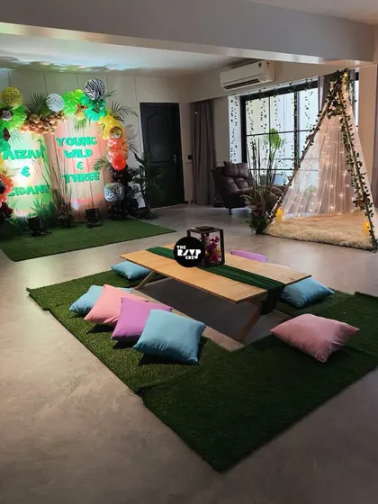 A cozy picnic-style setup for a 'Young, Wild & Three' party, with a low table and colorful cushions on an artificial grass mat.