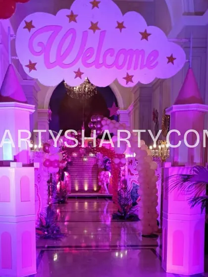A grand castle entrance designed in pink for a princess party. The setup includes castle turrets and a 'Welcome' sign on a cloud, setting a royal tone from the moment guests arrive.