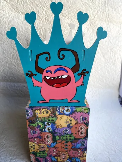 A front view of the monster-themed headband holder, showing the hand-painted pink monster on the crown-shaped side.