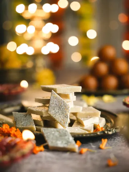 Kaju Katli with festive bokeh. This shot combines a classic Indian sweet with a magical, festive atmosphere, making it perfect for holiday campaigns.