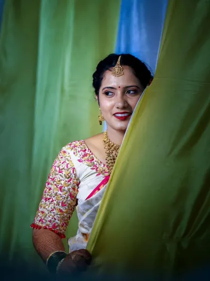 A playful and happy bride on her wedding day. The makeup is bright and fresh, with a pop of red on the lips that brings out the color in her embroidered blouse.