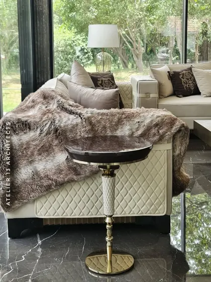 A detail from the Vasant Kunj glass house, showing a quilted leather sofa draped with a faux fur throw and a bespoke side table. This image captures the cozy, tactile elements we incorporate to make a space feel like home.