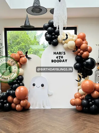 A spooky and fun "Booday" party for a 4th birthday. This Halloween-themed setup includes a cute ghost cutout, witch hats, and a black and orange balloon arch.