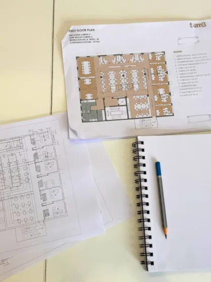 The architect's desk, showing floor plans and a blank sketchbook. This represents the continuous cycle of our work, moving between detailed technical drawings and the open possibilities of a new idea.