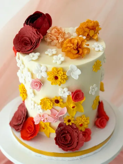 A celebration of color, this cake is fully covered in a variety of hand-piped buttercream flowers in warm shades of red, orange, yellow, and pink.