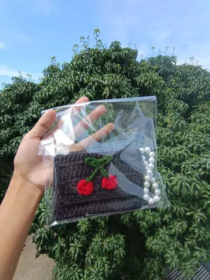 A black pocket purse with a cherry design and pearl strap, neatly packaged for a client's college fest.