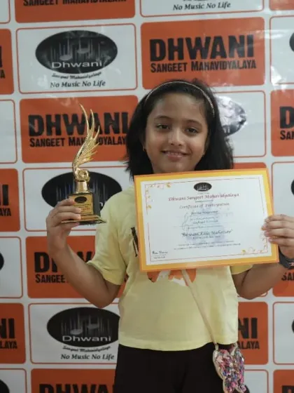 A young student beams with pride, holding her certificate and trophy.