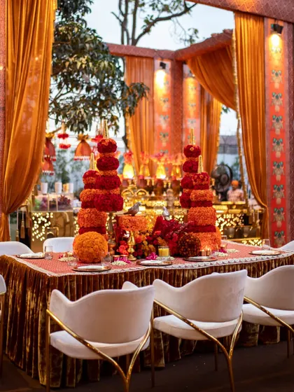 A tablescape featuring towering floral sculptures inspired by Indian temple architecture. The tiered structures are made from red and orange carnations and marigolds, creating a stunning visual impact.