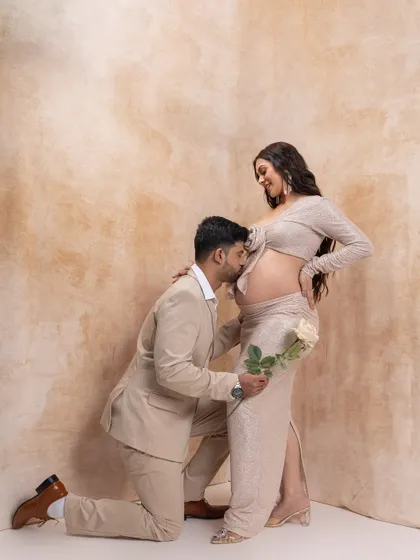 A gesture of love and promise. The father-to-be kneels to kiss his partner's belly, holding a white rose. This pose is a beautiful way to express devotion during a maternity photoshoot.