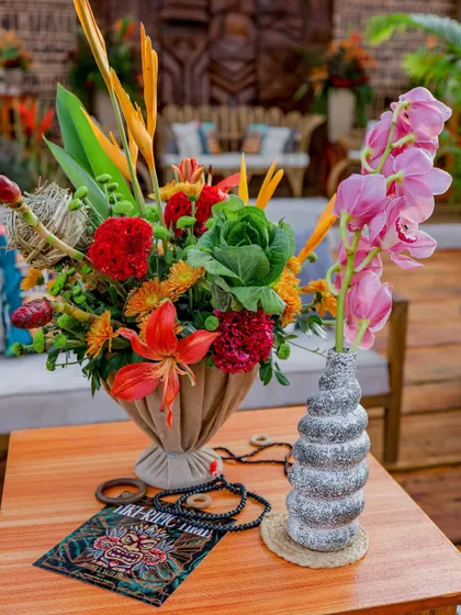 A beautiful arrangement of tropical flowers in a jute-wrapped vase, with a themed card in the foreground.